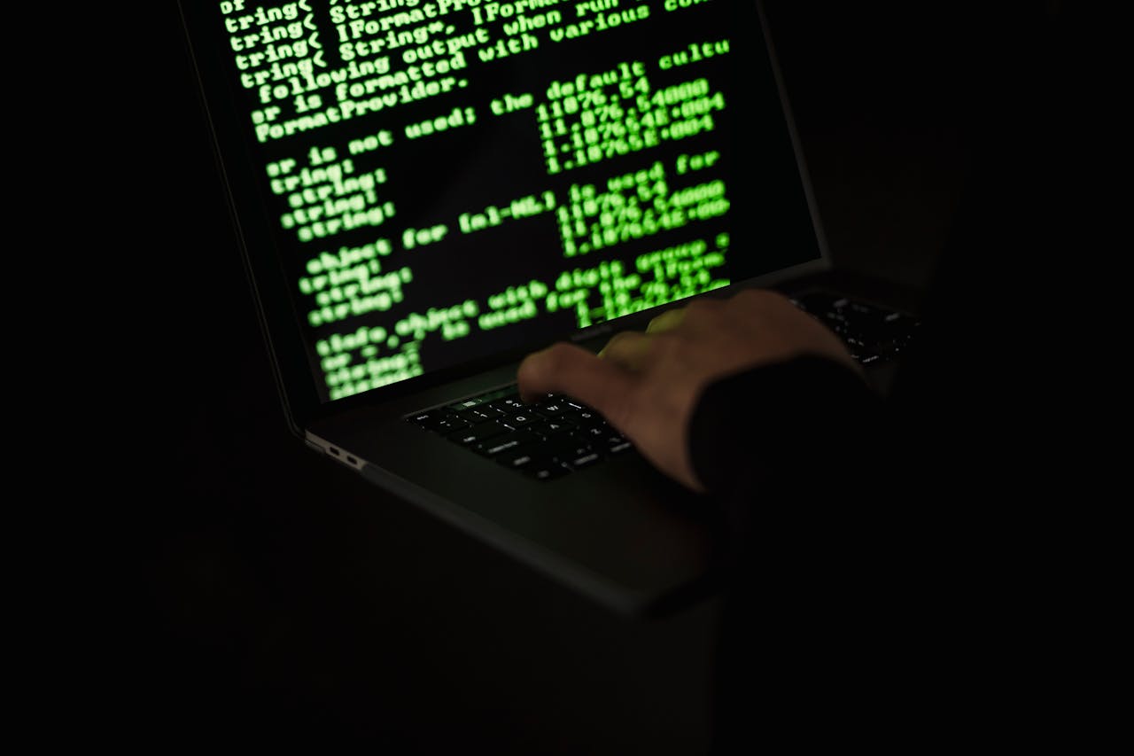 Servicios Silhouette of a hacker typing on a laptop in the dark with green code on screen.